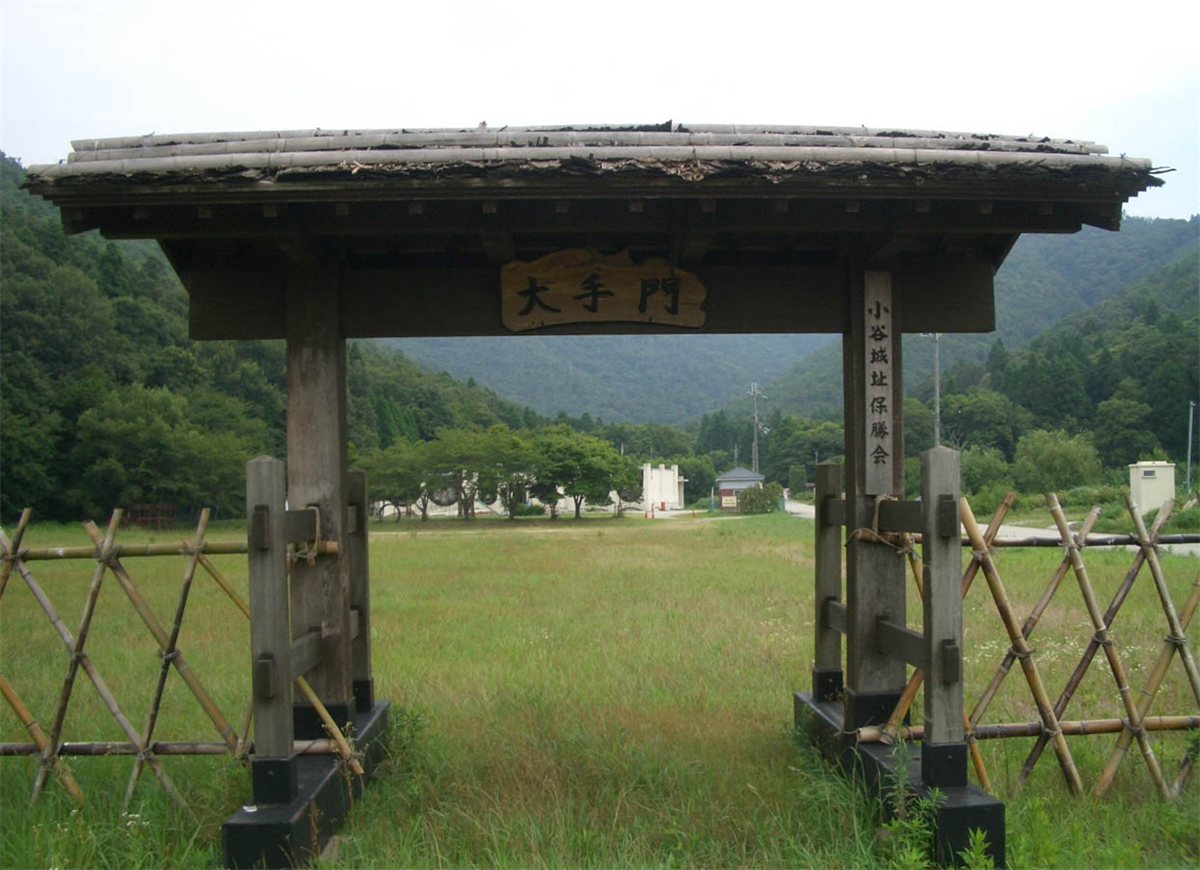 小谷城跡のふもとにある「大手門」の札をかけた木の門と、その奥に広がる草地と山