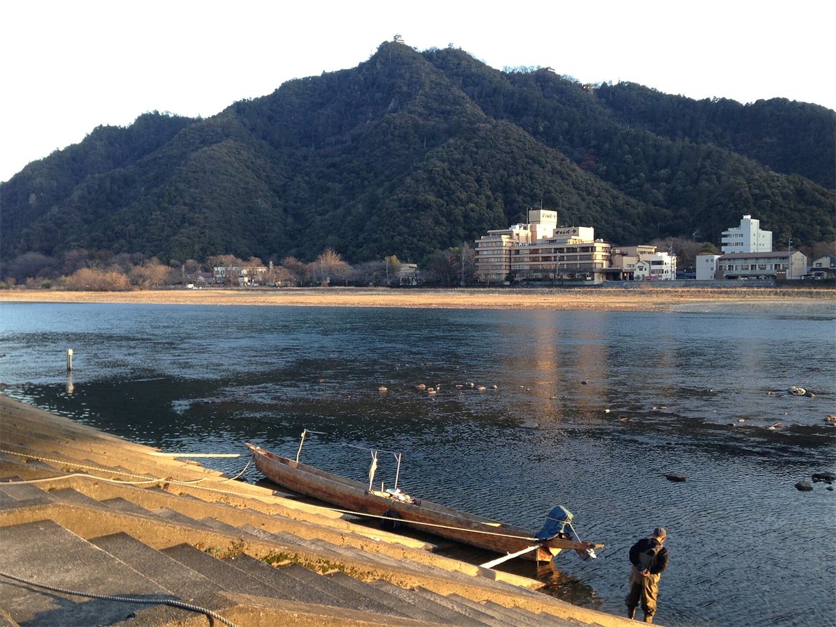長良川の岸の鵜舟と、川の向こうの金華山。山頂に岐阜城が見える